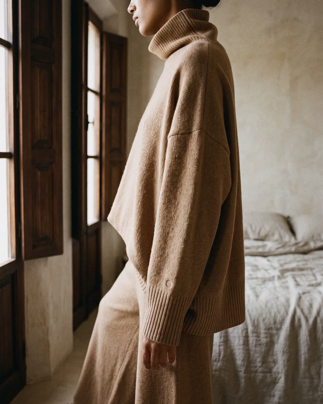 the cashmere set in dusk, a loose funnel-neck sweater and wide trousers, worn by a bedroom window