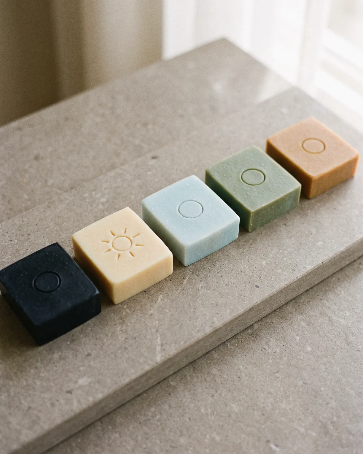 the five, one bar in each color, basalt, coconut cream, glacier, moss and dusk, in a row on a stone step by a window